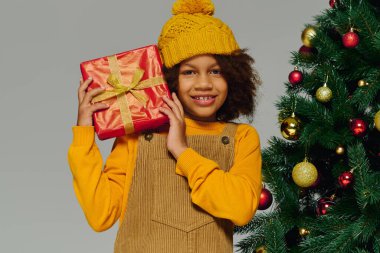Süslü bir Noel ağacının hediyesini taşıyan bir kız neşeyle ışıldıyor.