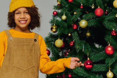 Neşeli bir kız Noel ağacına süslemeler ekliyor, tatil sezonunun ruhunu yakalıyor..