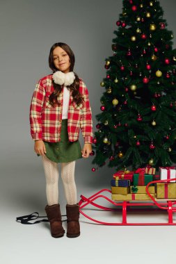 Neşeli kız, süslerle ve hediyelerle süslenmiş canlı bir Noel ağacının yanında duruyor.