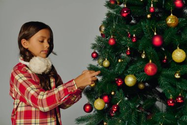 Neşeli kız, Noel ruhunu kutlayan Noel ağacına renkli süsler ekliyor..