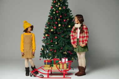 İki neşeli kız Noel ağacının yanında kahkahalarını ve hediyelerini paylaşıyor..