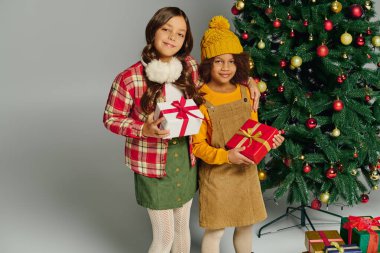 İki mutlu kız güzel dekore edilmiş bir Noel ağacının yanında hediyeler tutuyor..