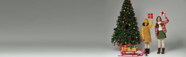 İki heyecanlı çocuk Noel 'in tadını güzel süslenmiş bir ağaç ve hediyelerle çıkarıyorlar..