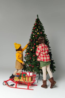 İki küçük bebek bir Noel ağacını süslerken sarılı hediyeler ve tezahüratlarla