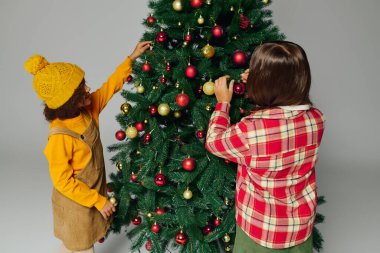 İki kız gülümseme ve kahkahaları paylaşırken bir Noel ağacına süs asar..