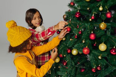 İki küçük çocuk Noel ağacına renkli süsler yerleştirip Noel ruhunu kutluyorlar..