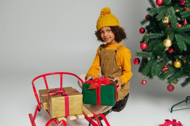Küçüğüm, güzel dekore edilmiş bir Noel ağacının yanında renkli hediyeler düzenlerken gülümsüyor..