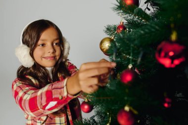 Neşeli kız, canlı süslemelerle dolu bir Noel ağacına süsler asıyor.