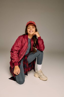 Şenlik kıyafetli küçük bir kız, pürüzsüz bir yüzey üzerinde diz çökerken ışıl ışıl gülümser..