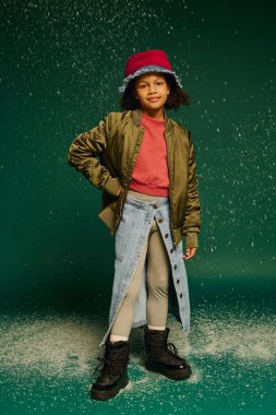 Küçük bir kız şık bir kıyafetin içinde neşeli bir şekilde poz veriyor, karlı havada neşeli bir anın tadını çıkarıyor..