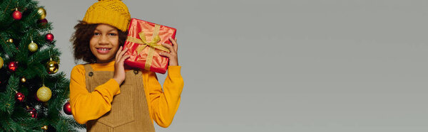 Young girl glows with joy, holding a beautifully wrapped gift at Christmas.