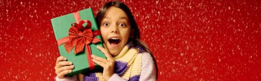 Mutlu bir kız, coşkulu bir Noel arkaplanının ortasında neşe saçan bir hediyeyi kucaklıyor..