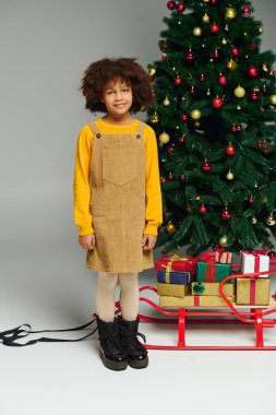 Neşeli bir kız güzel süslenmiş bir Noel ağacının yanında durur..