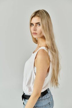 Kendine güvenen genç bir kadın, uzun sarı saçlarını ve günlük tarzını şık bir stüdyo ortamında sergiliyor..