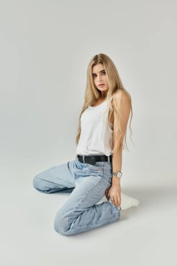 A young woman with long blonde hair poses in a studio, highlighting her casual fashion style. clipart