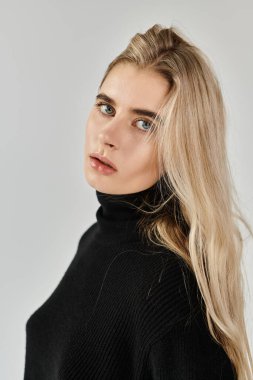 Çekici genç bir kadın, güzelliğini, sakin bir stüdyoda şık siyah bir elbiseyle sergiliyor..