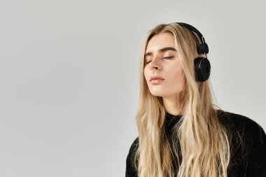 Uzun sarı saçlı genç bir kadın müzik dinlemekten zevk alıyor, modasını gösteriyor..