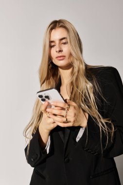 Uzun sarı saçlı genç kadın telefonunu kullanırken rahat bir şekilde siyah kıyafetler giyiyor..