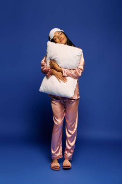 Güzel bir Afrikalı genç Amerikalı kadın neşeyle poz veriyor ipek pijama giymiş bir yastıkla.