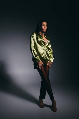 Zarif, Afro-Amerikan bir kadın yeşil ipek gömlekle rahatça poz veriyor..