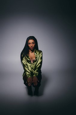 Güzel, genç, siyah bir kadın yeşil ipek bir gömlekle stüdyo arka planına poz veriyor..