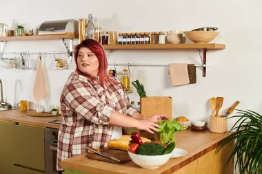 Plus size woman joyfully organizes fresh produce while preparing a healthy meal at home clipart