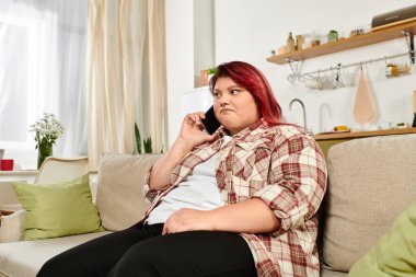 Comfortable woman engaging in a lively phone call while relaxing in her stylish living space clipart