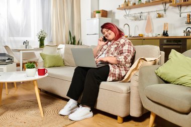 Young plus size woman smiles while chatting on her phone and typing away at home clipart