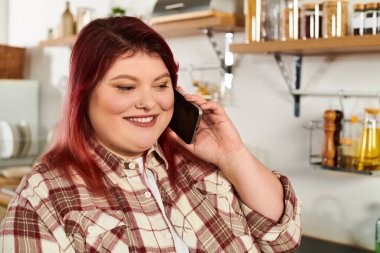 Parlak, davetkar bir mutfakta dururken, kızıl saçlı, gülümseyen bir kadın telefonda konuşuyor..