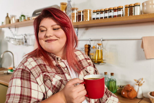 Молодая женщина с яркими волосами пьет кофе в красиво устроенной кухне, наполненной банками.