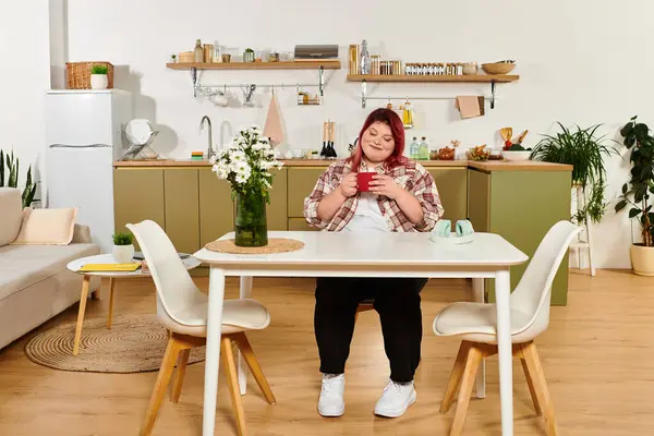 Genç ve iri yarı bir kadın şık bir mutfak masasında rahatlıyor ve içkisinin keyfini çıkarıyor..