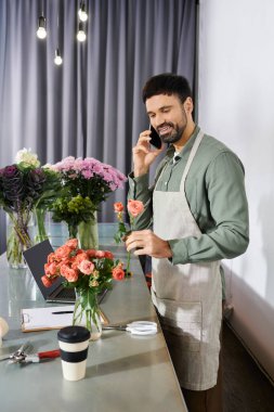 A bearded man engages with customers over the phone while crafting a beautiful bouquet. clipart