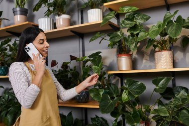 Genç bir çiçekçi dükkanında telefonla konuşurken bitkileri mutlulukla düzenliyor..