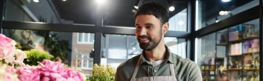 Yetenekli bir çiçekçi dükkanında sergilenen çiçekleri düzenlerken gülümser.