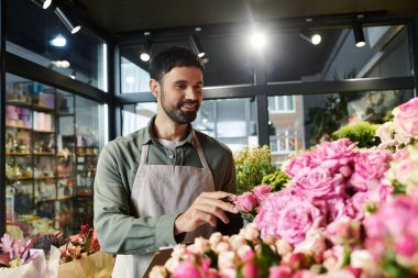 Handsome bearded man curates beautiful floral arrangements in his cozy shop. clipart