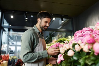 Sakallı bir adam, canlı çiçekçisinde sanatını sergilemek için taze çiçekleri dikkatlice düzenler..