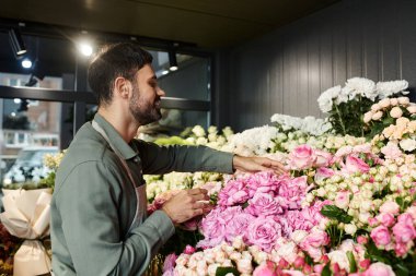 Yetenekli bir çiçekçi, dükkanındaki çeşitli çiçeklerin arasında büyüleyici pembe güller düzenler..