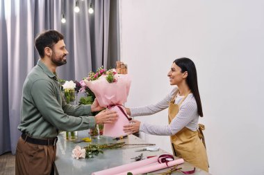 Bir çiçekçi mağazadaki erkek müşterisine coşkuyla muhteşem bir buket sunar..