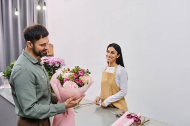 A talented florist engages with a male client while showcasing a stunning bouquet of flowers. clipart