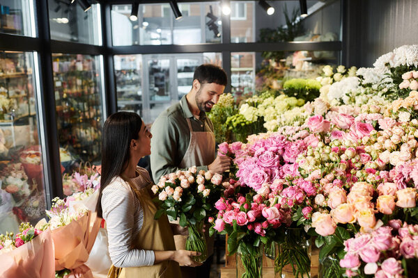 A married couple joyfully arranges beautiful roses and plants in their florist shop.