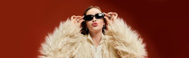 Canlı stil sahibi bir kadın, güneş gözlüğü ve kabarık bir paltoyla neşeli poz verir..