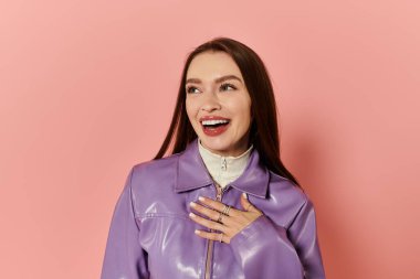 Güzel bir kadın pembe bir arka plana karşı mor bir ceketle neşe saçar..