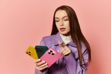 Renkli telefon kılıflı şık bir kadın, pembe arka planda telefonuyla iletişim kuruyor..