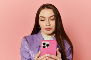 Uzun saçlı şık bir kadın akıllı telefonunu pembe bir fon üzerinde kullanır..