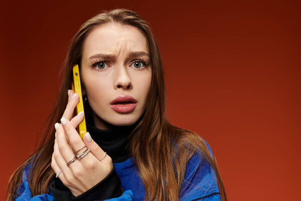 Beautiful woman with long, wavy hair expresses surprise while holding a yellow phone.