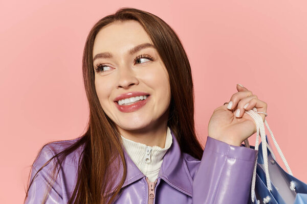 Stylish woman beams with joy, showcasing her trendy outfit while holding a colorful bag.
