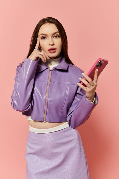 Красивая женщина с длинными волосами носит фиолетовый наряд и держит смартфон во время позирования.