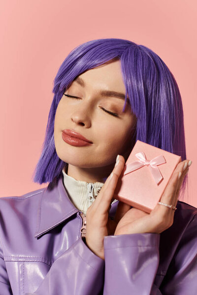 Улыбающаяся женщина с фиолетовыми волосами игриво держит розовую подарочную коробку.