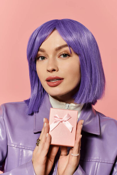 Стильная женщина с фиолетовыми волосами уверенно улыбается розовой подарочной коробкой на розовом фоне.