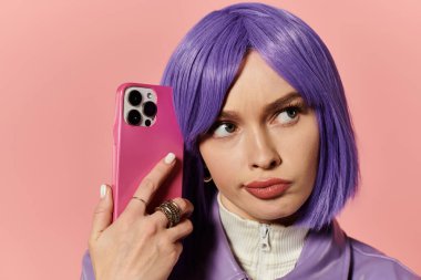 Mor peruklu kendine güvenen bir kadın pembe bir telefon tutarken tarzını sergiliyor..